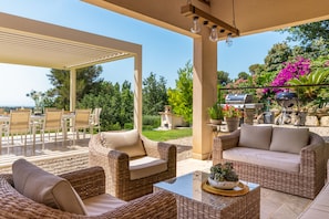 An outdoor patio with wicker furniture, a glass table, and a barbecue grill. - Le Roucasset – Pool & sea view (Tourrettes-sur-Loup)
