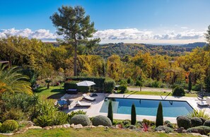 A swimming pool surrounded by a well-maintained garden with various plants and a clear view of the forest in the background. - Le Roucasset – Pool & sea view (Tourrettes-sur-Loup)