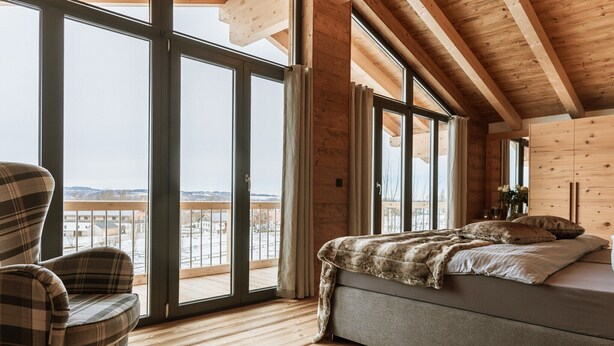 Una camera da letto con un'ampia porta-finestra che si apre su un balcone, un letto con coperta e una poltrona a quadri.