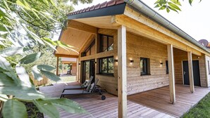 A wooden cabin with a deck, large windows, and a covered outdoor seating area. - Ebenerdiges gemütliches Chalet im Vital Camp Bayerbach (Bayerbach)