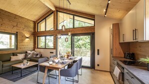 A modern kitchen with wooden cabinetry, a dining area with a table and chairs, and large windows allowing natural light. - Ebenerdiges gemütliches Chalet im Vital Camp Bayerbach (Bayerbach)