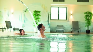 En indendørs swimmingpool med klart vand, en person der svømmer, og en anden person i baggrunden.