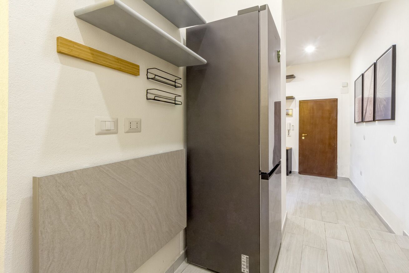 A modern kitchen with a stainless steel refrigerator, a wooden shelf, and a light switch on the wall.