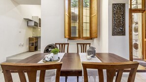 A dining area with a wooden table and chairs, a window with wooden shutters, and a decorative wall piece. - Carlo's Apartment | Near the train and bus station | 2 minutes from the city center | Free Netflix and Wi-Fi (Sassari)