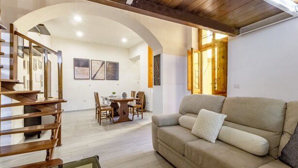 A living room with a sofa, wooden staircase, dining table, and chairs. - Carlo's Apartment | Near the train and bus station | 2 minutes from the city center | Free Netflix and Wi-Fi (Sassari)
