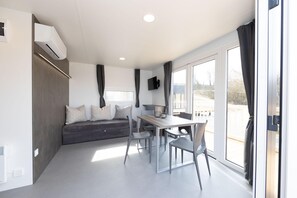 A modern room with a sofa, dining table, chairs, a flat-screen TV, and a large window. - Familienfreundliches MobileHome im Vital Camp Bayerbach (Bayerbach)