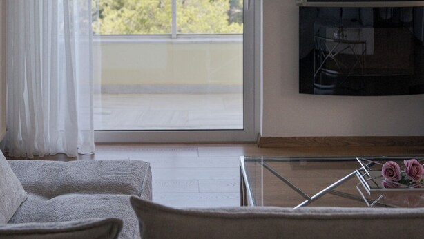 Ein Wohnzimmer mit großem Fenster, einem Wand-Fernseher und einer Couch.