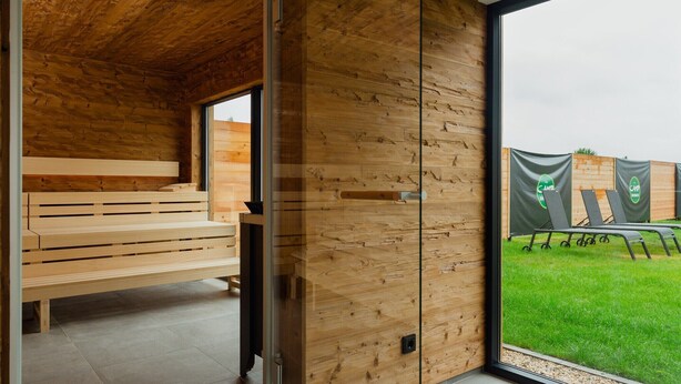 Un intérieur moderne avec des murs lambrés en bois, un banc et une vue sur un espace extérieur avec de l’herbe verte et une clôture.