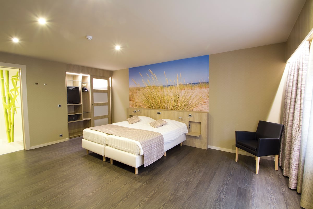 Ein Schlafzimmer mit Bett, Sessel, Kleiderschrank und einem Gemälde an der Wand.