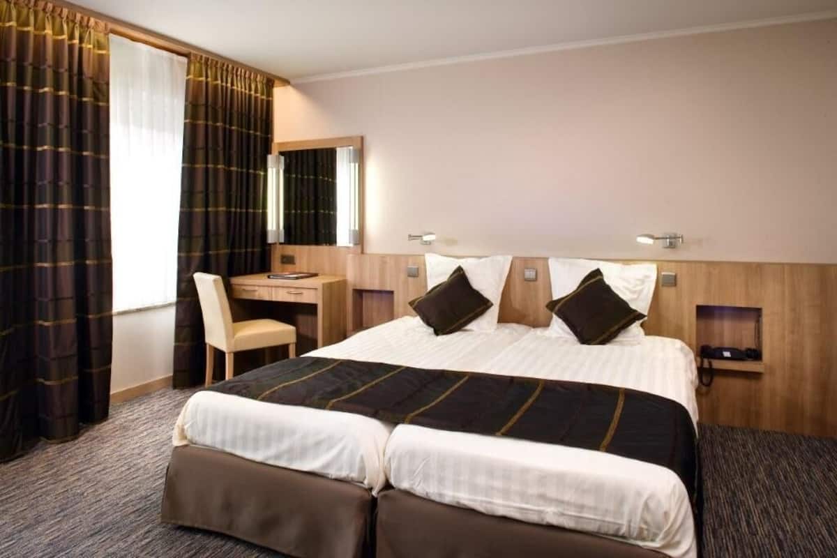 Une chambre d’hôtel avec un grand lit, un bureau, une chaise, un miroir et une petite étagère sur laquelle se trouve un téléphone.