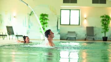 Una piscina interior con agua cristalina, una persona nadando y otra al fondo.