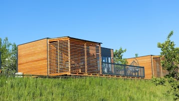 Una cabaña moderna de madera con revestimiento de listones y un balcón, ubicada en un campo cubierto de hierba.