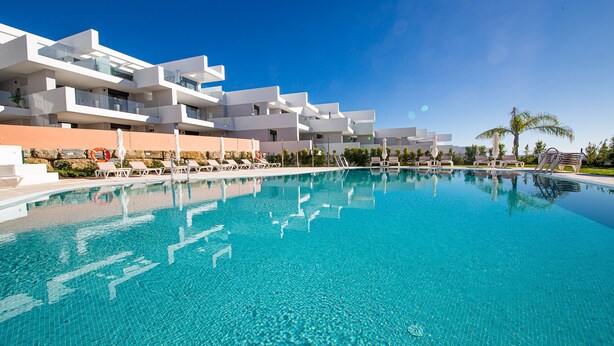 A modern hotel with a large swimming pool, multiple balconies, and outdoor seating areas. - Pure South apartment 11.2a (Manilva)