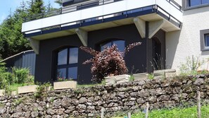 Een modern herenhuis met een stenen muur, grote ramen en een tuin met diverse planten.