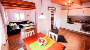 A cozy interior with a wooden ceiling, a dining area with a table and chairs, a kitchen with white cabinets, and a living area with a sofa and a window.