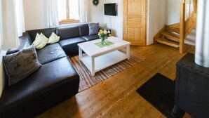 A living room with a black leather sofa, a white coffee table with a vase of flowers, wooden flooring, a wooden staircase, and a black heater.