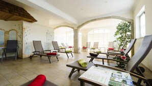 A spacious indoor area with multiple lounge chairs and tables, stone arches, and large windows allowing natural light.