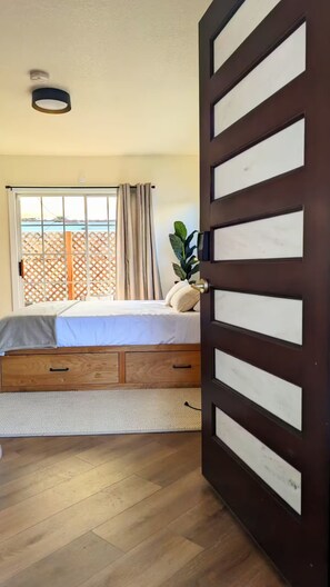 A bedroom with a bed, a window with curtains, a wooden floor, and a door with a handle. - Charming Tiny Unit LA w/HotTub (Los Angeles)