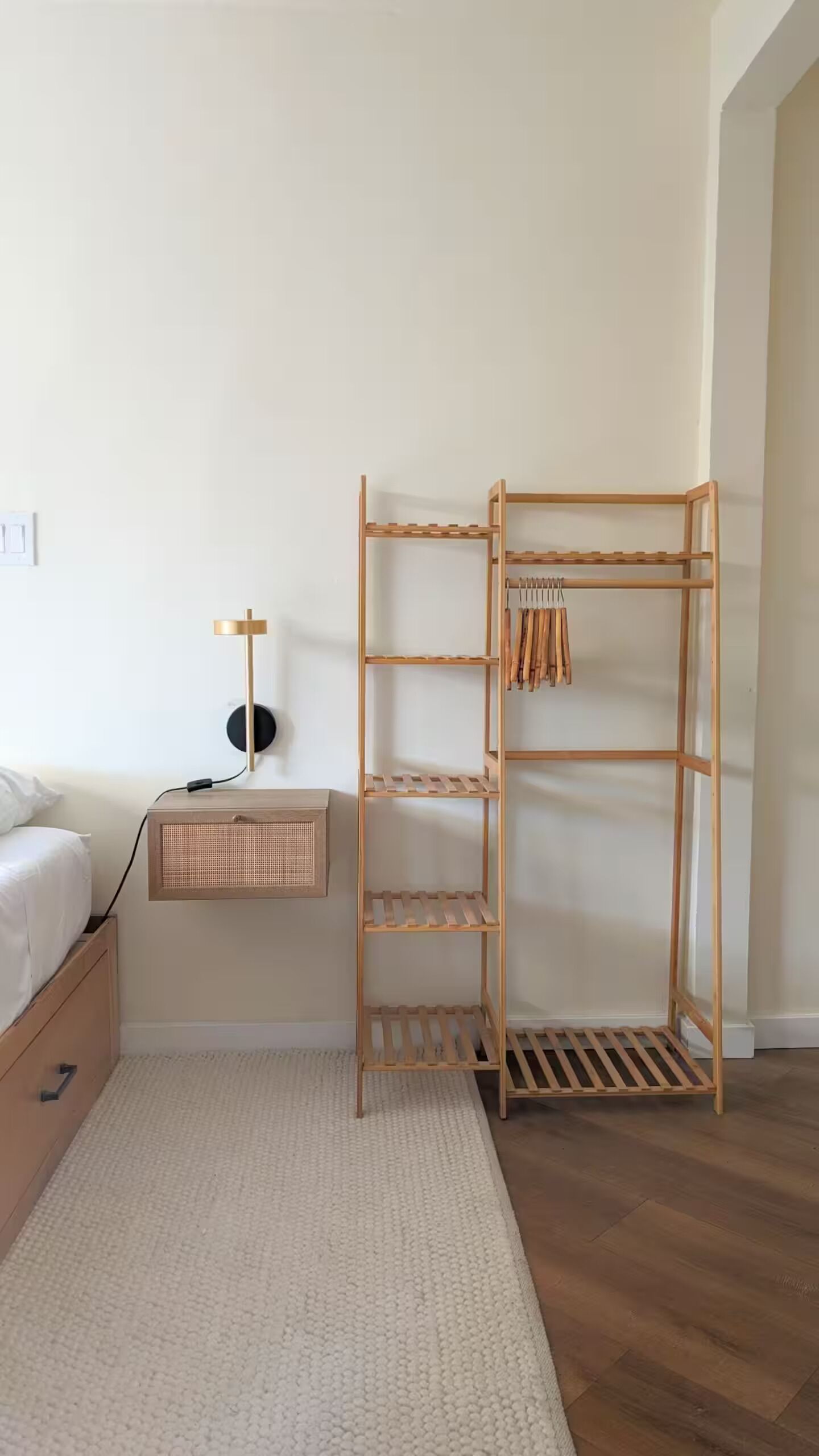 A bedroom with a wooden wardrobe, a bedside table, a lamp, and a white rug.