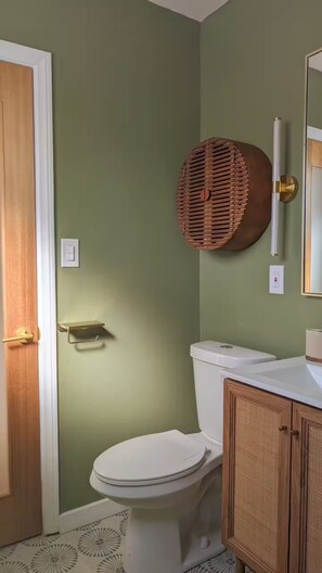 A bathroom with a toilet, a wooden cabinet, and a wall-mounted basket. - Charming Tiny Unit LA w/HotTub (Los Angeles)