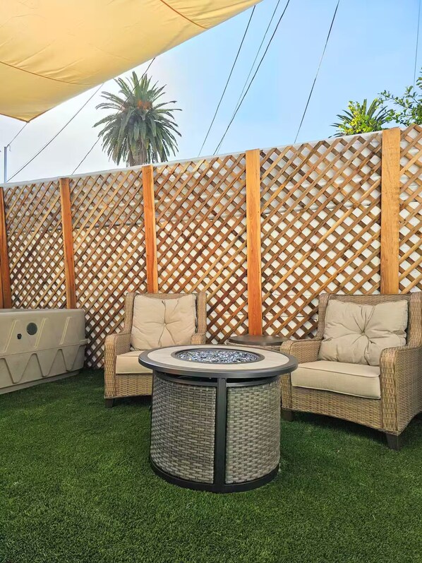 A patio area with two wicker chairs, a round table with a built-in fire pit, and a decorative wall with a lattice pattern. - Charming Tiny Unit LA w/HotTub (Los Angeles)