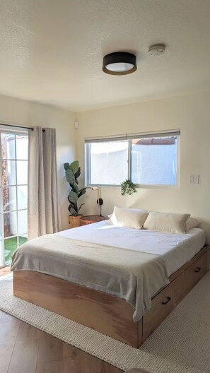 A bedroom with a large bed, a window with a view, a ceiling light, and a plant. - Charming Tiny Unit LA w/HotTub (Los Angeles)