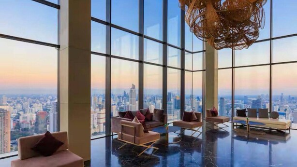 A high-rise interior with large windows offering a city view, modern seating, and a polished floor. - Circle Living Skyline Residence (Bangkok)