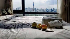 A bedroom with a bed, a nightstand, and a view of a cityscape through a large window. - Circle Living Skyline Residence (Bangkok)