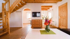 A wooden staircase, a flat-screen TV, a wooden dresser, and a vase with flowers on a white table. - Familienfreundliches Feriendomizil im Landhausstil im Vital Camp Bayerbach (Bayerbach)