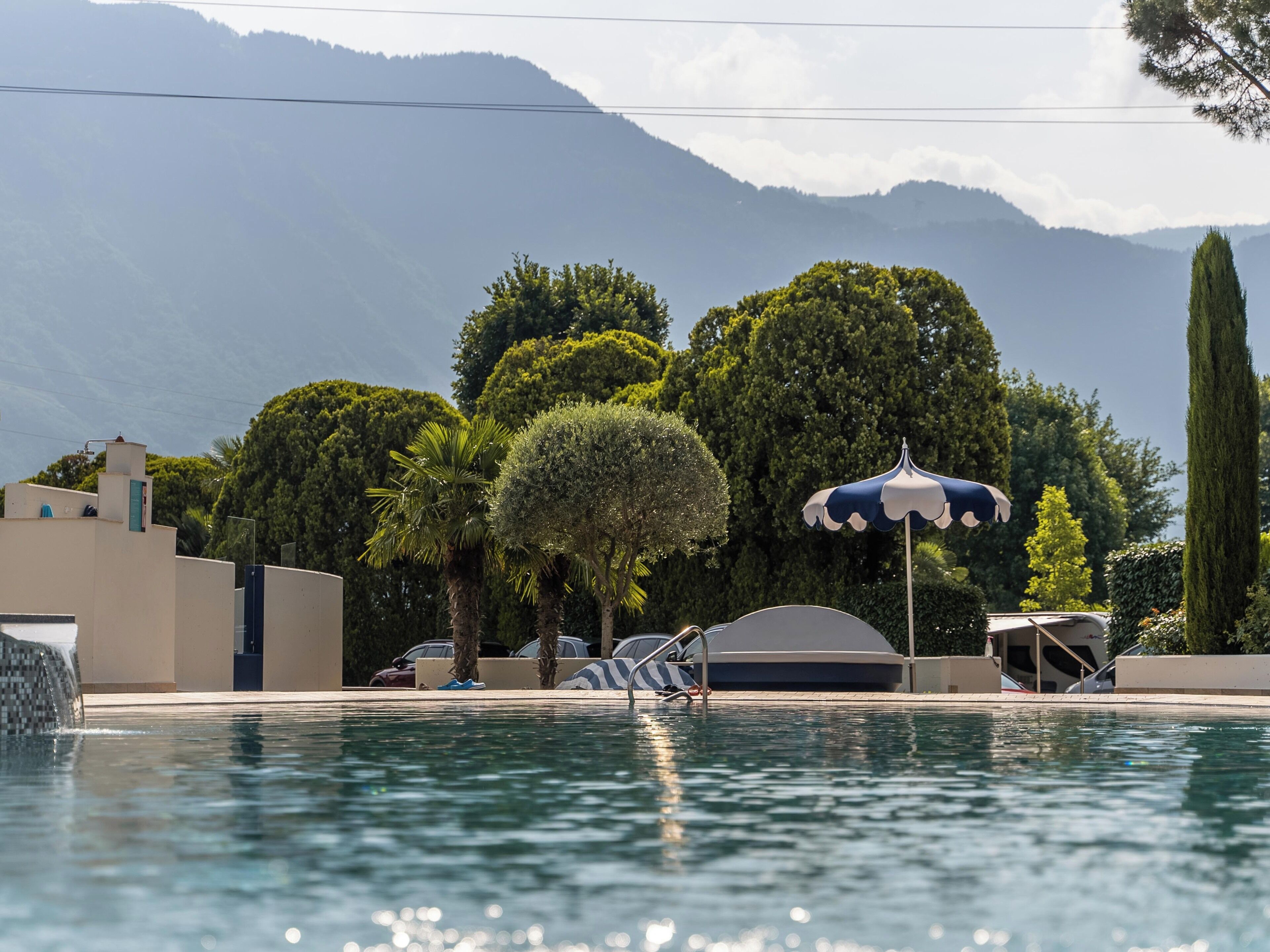 Una piscina con le montagne sullo sfondo, circondata da vegetazione rigogliosa e un cielo sereno.