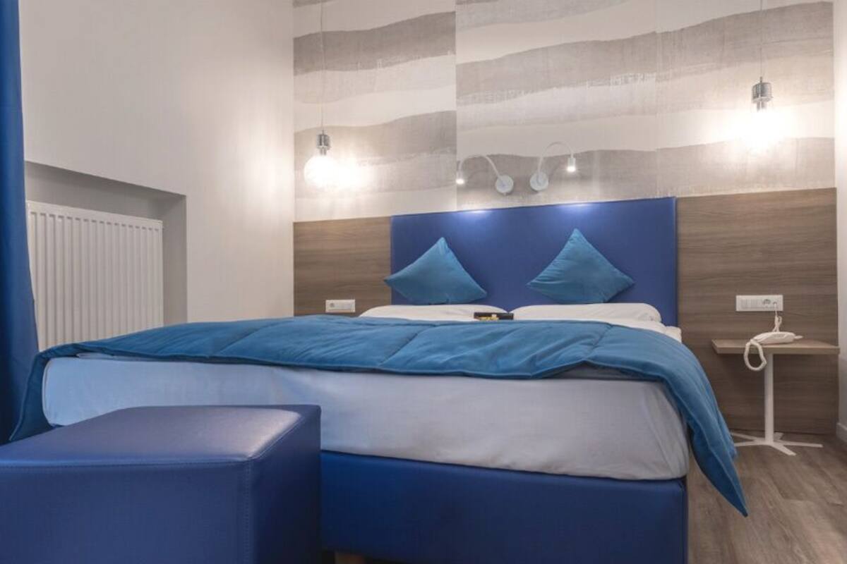 A modern hotel room with a large bed, a bedside table, a mirror, and a blue accent wall.