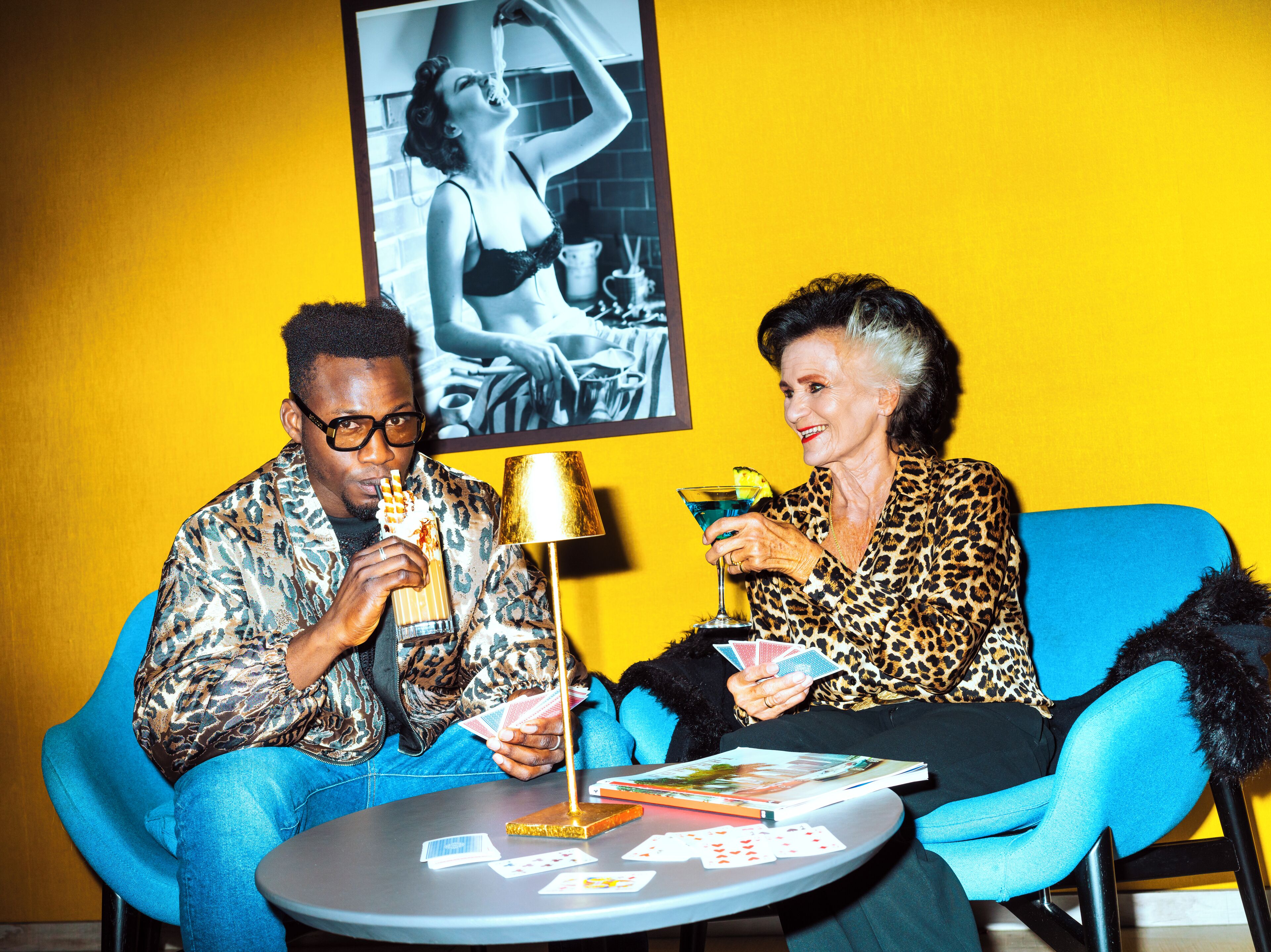 Two people playing cards at a table with a lamp and a magazine.