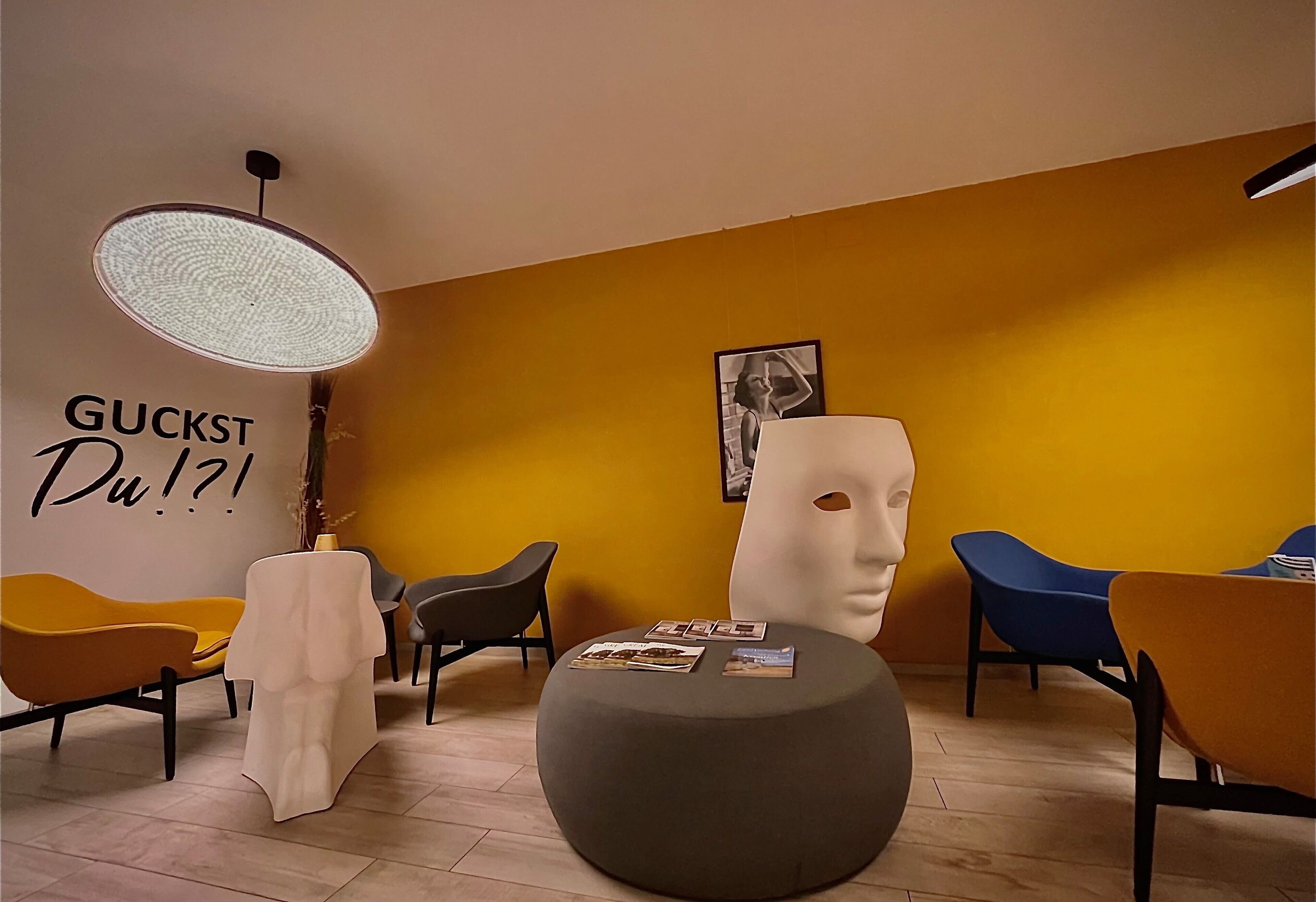 Un interno moderno con una parete gialla a contrasto, una parete bianca con scritte e un pouf rotondo con riviste.