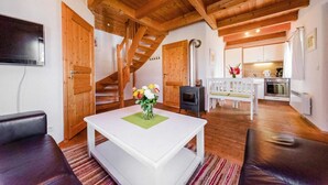 Ein gemütliches Wohnzimmer mit einem weißen Tisch, einer Couch, einer Holztreppe und einer Küchenzeile mit Herd.