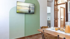 Un comedor con una mesa dispuesta para el desayuno, un televisor montado en la pared y una puerta que da a otra habitación.