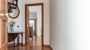 Un pasillo con una puerta de madera, un espejo y un jarrón con flores.