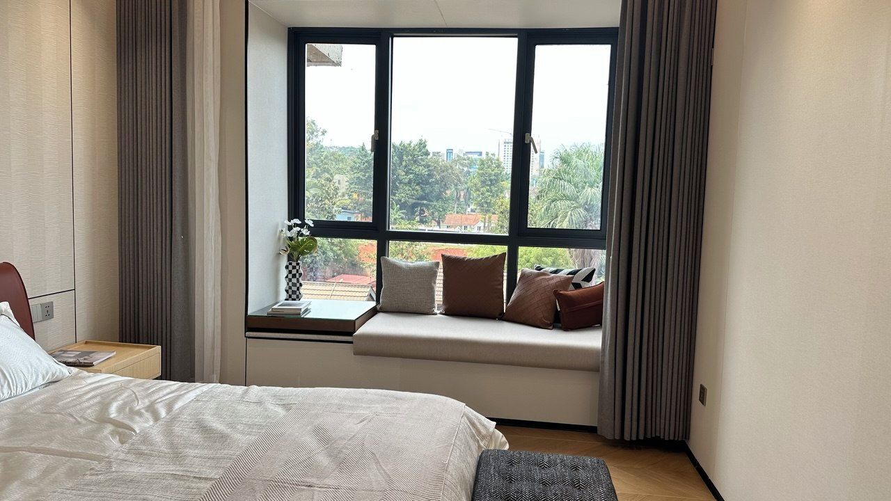 Una habitación de hotel con una cama grande, un asiento junto a la ventana con cojines y vistas a la ciudad.