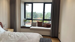 A hotel room with a large bed, a window seat with cushions, and a view of the cityscape. - Larose Royal Apartments (Kampala)