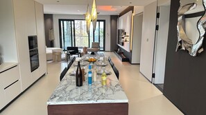 A modern kitchen with a marble island, built-in appliances, and a dining area with a large window. - Larose Royal Apartments (Kampala)