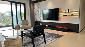 A modern living room with a flat-screen TV, seating, a fireplace, and a view of the outdoors.
