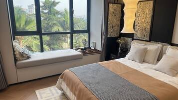 A hotel room with a large bed, a window seat, a nightstand, and a lamp.
