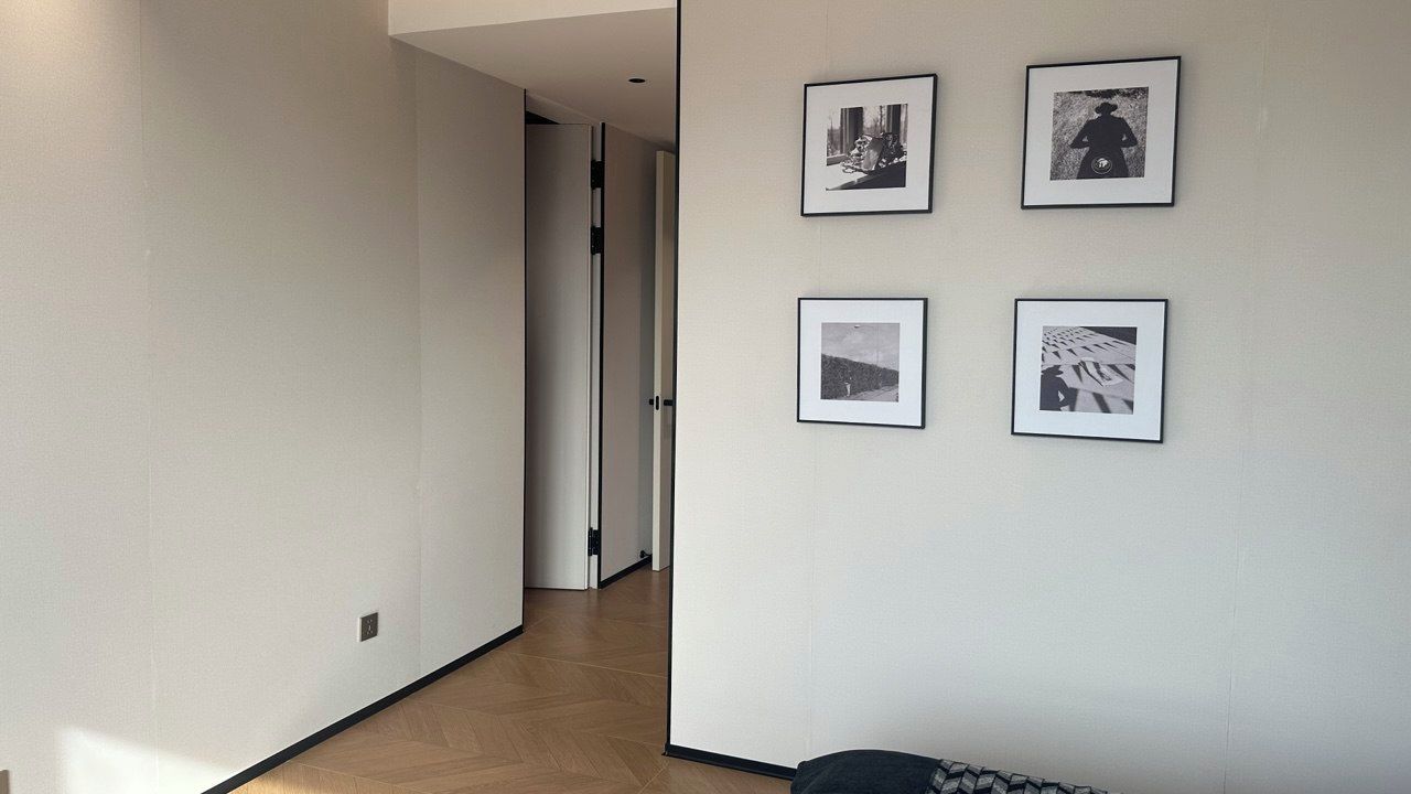 Un pasillo con piso de madera, una puerta al final y cuatro cuadros en la pared.