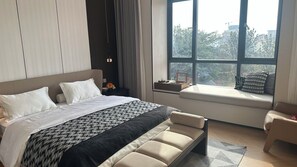 A modern bedroom with a large bed, a window seat, and a view of the city.