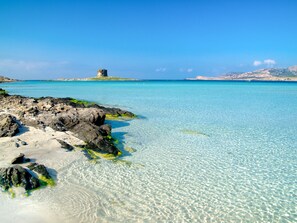 A coastal scene with clear turquoise waters, rocky shoreline, and a distant island with a structure. - Shaloma by Interhome (Stintino)