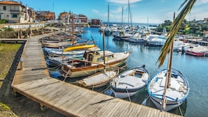 A marina with various boats docked along a wooden pier, surrounded by buildings and a clear sky.