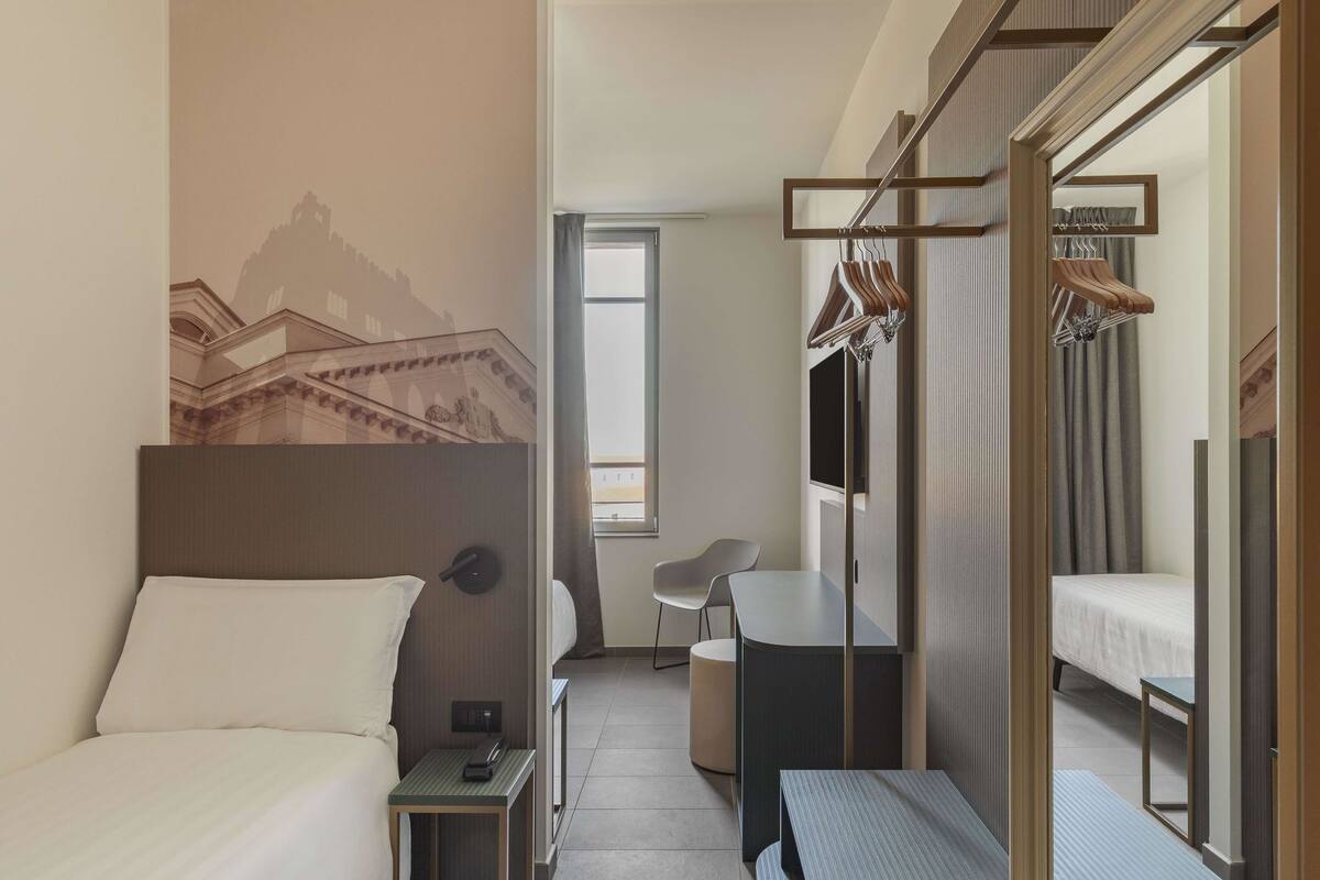 Een hotelkamer met een bed, een bureau, een stoel, een kast en een spiegel.