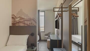 A hotel room with a bed, a desk, a chair, a wardrobe, and a mirror.
