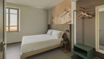 A hotel room with a bed, a small table, a mirror, and a wall-mounted coat rack.