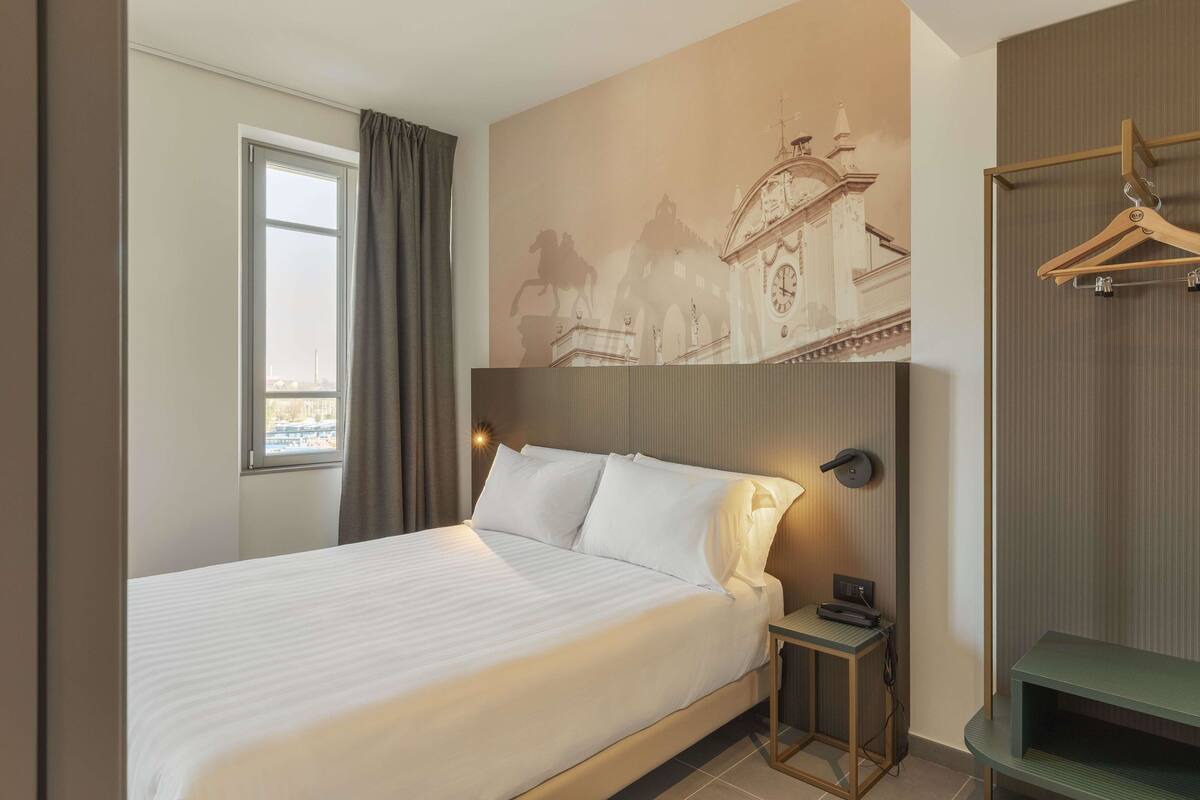 Een hotelkamer met een bed, een nachtkastje, een tv aan de muur en een kapstok.
