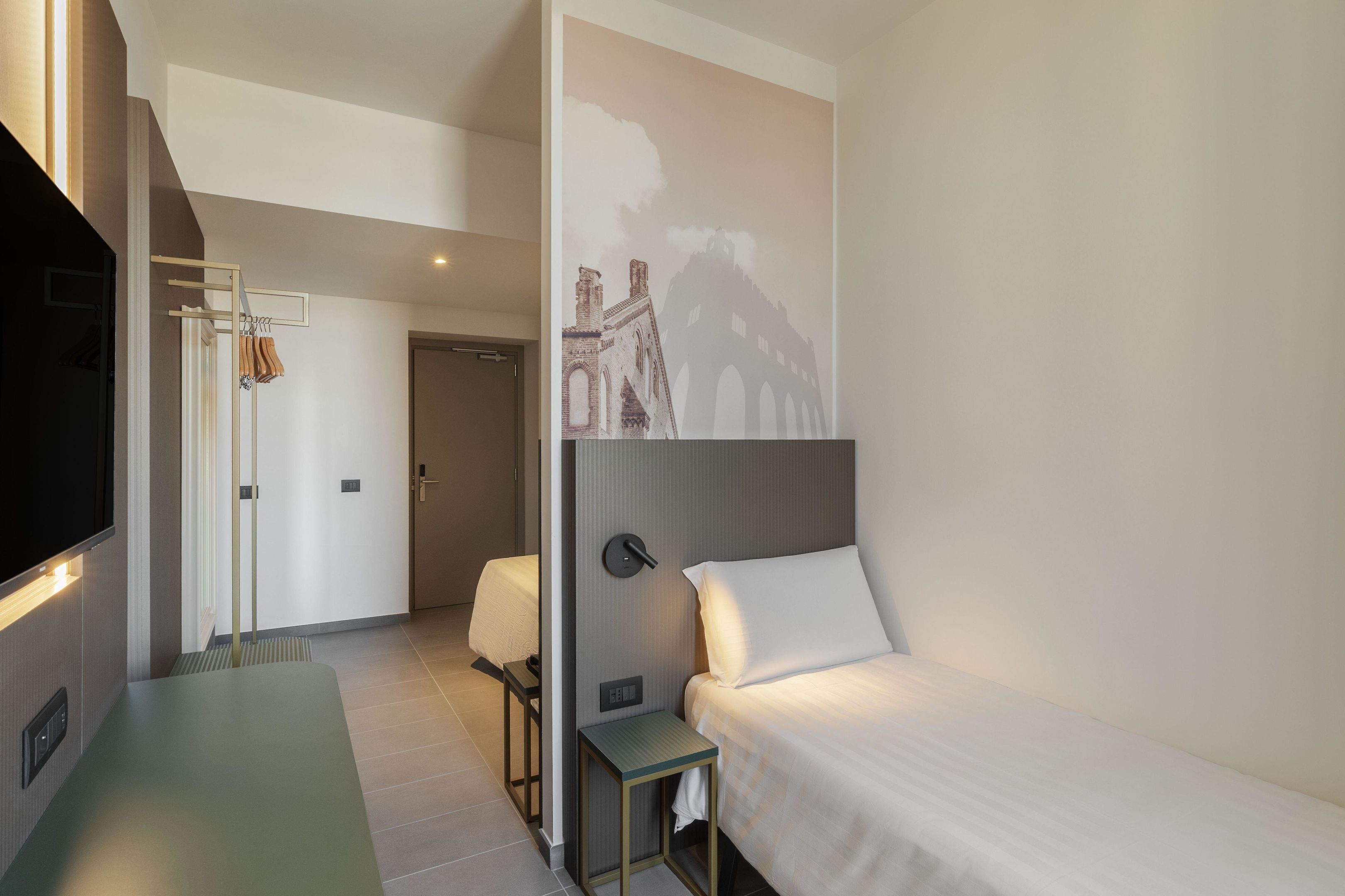 A hotel room with a bed, a desk, a chair, a TV, and a wall with a mural.